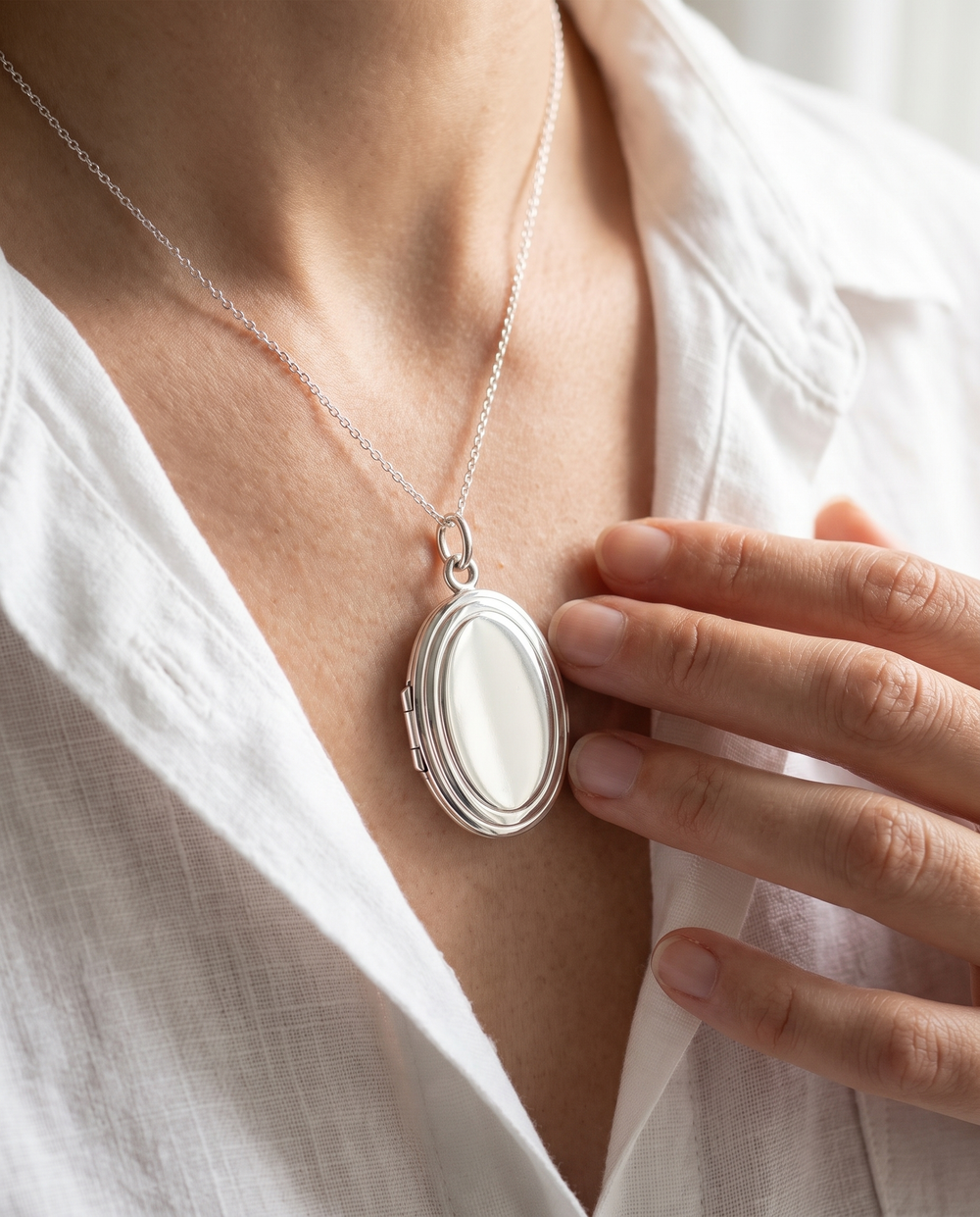 Médaillon Ovale en argent porté sur une chaîne fine, chemise en lin blanc