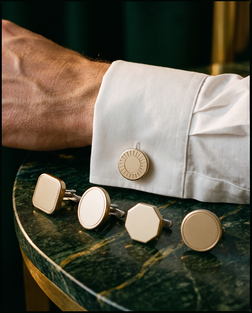 Bouton de manchette Hero à tête Rayons porté sur une chemise blanche, avec quatre autres têtes interchangeables posées sur du marbre vert